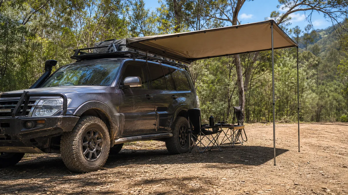 White 4x4 camp vehicle with a side awning open under trees.