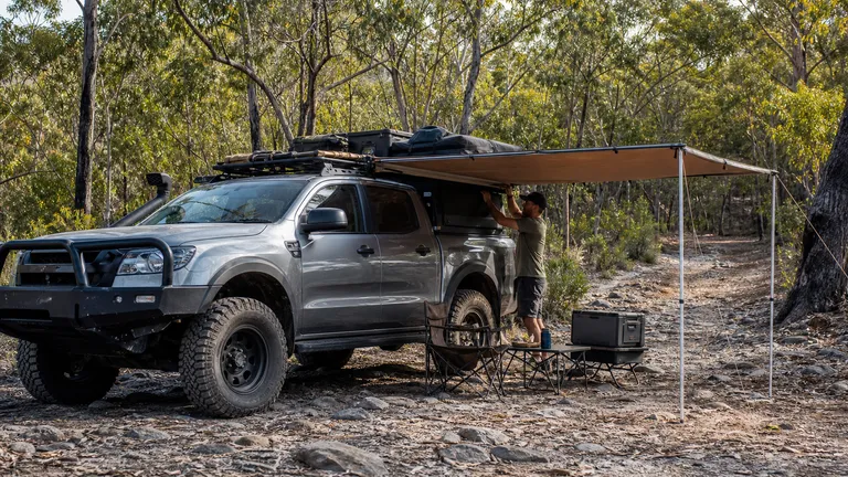 4x4 pickup on a rocky trail with a side awning case mounted on the rack.