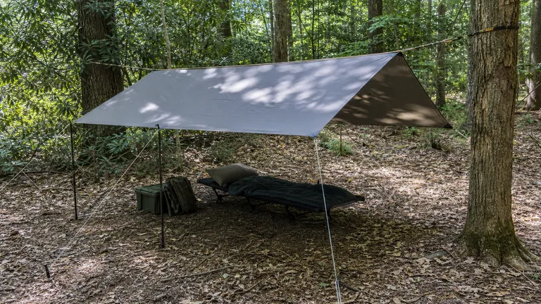 Tarp shelter pitched in the woods with poles and a ridgeline.