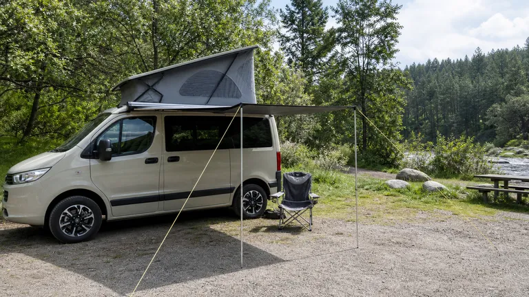 Small campervan with pop-up roof, deployed side awning and a camp chair beside the van.